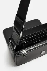 Bandolera negra con acabado grabado, compartimento principal con cierre mediante solapa imantada, bolsillo interior con cierre mediante cremallera, bolsillo frontal con cierre mediante cremallera, asa de hombro ajustable y monedero.