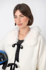 Cardigan blanco de lana con cuello de piel sintética, cierre frontal con lazos de terciopelo negro y corte holgado.