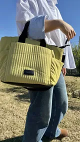 Cartera negra tipo tote bag con diseño capitoneado, doble asa corta y correa larga ajustable. Incluye bolsillos laterales y bolsillo frontal amplio.