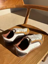 Championes urbanos de cuero color blanco hueso con detalles en marrón. Presentan cordones de algodón color crudo y logo bordado en el lateral.