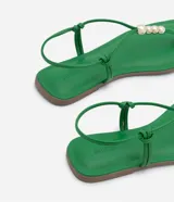 Sandalia plana color verde con tiras finas, cierre en el tobillo, punta cuadrada y detalle de esferas doradas.