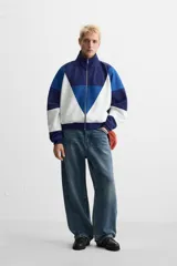 Chaqueta deportiva azul marino, azul y blanca con cierre frontal, cuello alto y bolsillos laterales.