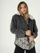 Campera de jean gris oscuro con cuello de piel sintética blanca, cierre frontal con cremallera, bolsillos laterales y puños con cremallera.