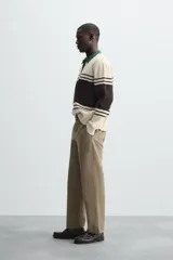 Polo de hombre relaxed fit, tejido en hilatura con textura chenilla. Presenta cuello solapa con cierre frontal de botonadura, manga larga y acabados en rib. Diseño a rayas horizontales en color crema y negro, con cuello en verde oscuro.