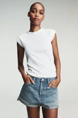 Shorts de jean de algodón, tiro alto, color azul claro desgastado. Presenta cinco bolsillos, cierre frontal con botón metálico y bajo desflecado con vuelta.