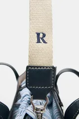 Bolso shopper azul marino con doble asa corta y correa larga de tela color crudo. Tiene detalle de pespuntes blancos y tira con anilla metálica.