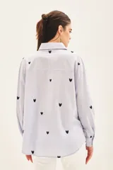 Camisa blanca de algodón con bordado de corazones dorados, corte amplio, cuello clásico, cartera con botones ocultos y bolsillo en el pecho.