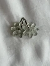 Par de aros plateados con forma de flor con glitter.
