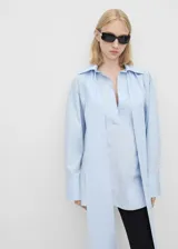 Camisa celeste de algodón, corte oversize, con cuello camisero, mangas largas con puños abotonados y cierre de lazo en el cuello.