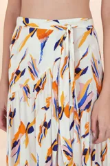 Falda pareo larga de caída fluida, con estampado abstracto en tonos naranja, azul y rosado sobre fondo blanco. Diseño cruzado con amarre lateral y corte asimétrico con volado.