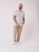 Camisa de hombre de manga corta con cuello cubano y estampado de rayas verticales en tonos beige, azul y rojo. Tiene un bolsillo en el pecho.