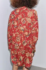 Camisa larga de algodón con estampado floral en tonos rojos, marrones y verdes. Tiene cuello solapa, manga larga con puños y bajo redondeado.