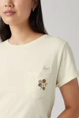 Remera color crema de corte recto, con mangas cortas con dobladillo y bolsillo en el pecho con bordado floral.