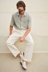 Camisa color verde claro con cuello inglés, tapeta lisa y canesú en la espalda. Modelo de manga corta con dos bolsillos superiores abiertos y bajo recto con aberturas laterales.