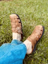 Sandalias suecos color camel con tiras de cuero trenzado, hebilla metálica y suela de goma negra.