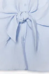 Camisa celeste de manga corta con cuello solapa y cierre frontal con botones. Tiene un nudo en la parte delantera.