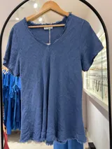 Remera de manga corta color azul jean, con cuello en V deshilachado y ruedo con terminación deshilachada.