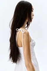 Vestido corto blanco de popelina de algodón, con breteles finos que se atan en moño, escote corazón y falda acampanada con volado en el ruedo.