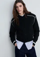 Chaqueta bomber de punto color negro con cierre de botones a presión, cuello redondo y bolsillos ribeteados. Presenta ribetes blancos en contraste en hombros y puños.