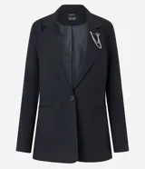 Blazer negro de sastrería con corte alargado, cuello con solapa, manga larga, botón delantero, bolsillos fake y cadena decorativa en la solapa.