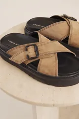 Sandalias planas color beige con tiras cruzadas y hebilla decorativa.