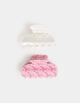 Set de dos broches para el pelo tipo pinza. Uno es de color blanco perlado con apliques de perlas sintéticas formando un moño. El otro es de color rosa con estampado de moños en rosa más oscuro.