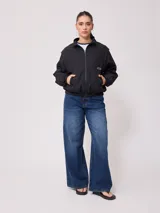 Campera negra tipo rompevientos de nylon con cierre frontal y bolsillos laterales.