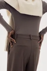 Pantalón sastrero marrón de corte holgado con tiro alto y cierre con corchete y botón ocultos. Piernas amplias con pinzas, pliegues adelante y atrás, bolsillos al bies y bolsillos decorativos atrás.