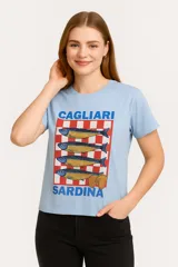 Remera celeste de manga corta y cuello redondo, con estampado de sardinas sobre fondo a cuadros rojos y blancos. Incluye texto con los nombres de las ciudades de Cagliari y Sardina.