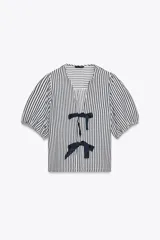 Blusa de cuello redondo con escote pico y manga corta abullonada acabada en elástico. Cierre frontal con lazos. Diseño a rayas verticales blancas y negras.