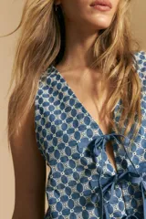 Chaleco corto sin mangas, color azul con estampado geométrico en blanco. Presenta escote en V pronunciado y lazos ajustables en el centro frontal.