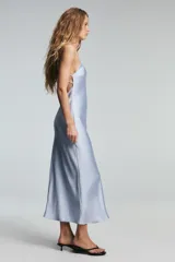 Vestido midi negro de tejido satinado, con escote en pico y tirantes finos ajustables. Presenta un detalle de tiras cruzadas en la espalda descubierta y cierre con cremallera metálica.