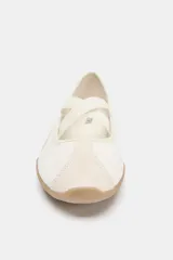 Zapato plano tipo bailarina deportiva, color blanco hueso, con puntera redonda y suela engomada marrón claro. Presenta tiras elásticas cruzadas en el empeine y detalles en gamuza clara.