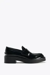 Zapato tipo mocasín de charol negro, con detalle de antifaz en el empeine y punta redonda.