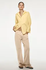 Camisa amarilla de popelina de algodón, con cuello solapa, escote en pico, manga larga con puños y cierre frontal con botones.