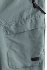 Pantalón jogger deportivo color verde grisáceo, con cintura elástica ajustable con cordón, bolsillos laterales con cierre, bolsillos cargo con solapa y bajos elásticos.