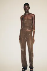 Pantalón semitransparente color marrón chocolate, de tiro medio y corte recto. Presenta aplicación de abalorios y lentejuelas plateadas con motivos geométricos y florales. Incluye short interior a tono.
