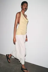 Vestido largo de fiesta con cuello halter fluido y hombros descubiertos. Presenta un top dorado drapeado y una falda larga color crema con textura.