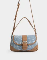 Bandolera de denim celeste con estampado floral blanco, detalles en cuero sintético marrón y correa de hombro ajustable. Cierre con hebilla metálica.