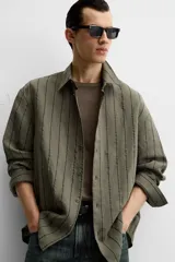 Camisa de hombre regular fit, color blanco con rayas verticales negras, cuello solapa, manga larga con puños abotonados y cierre frontal con botones.