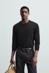 Jersey negro de lana con acabado mercerizado, corte relaxed fit, cuello redondo y mangas largas con terminaciones en rib.