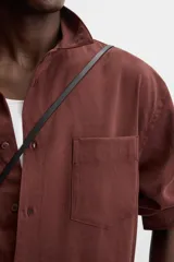 Camisa color borgoña de corte relajado, confeccionada en tejido con mezcla de viscosa. Tiene cuello solapa, manga larga con puños abotonados, bolsillo de parche en el pecho y cierre frontal con botones.