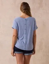 Remera celeste de corte recto, con cuello redondo y mangas cortas con dobladillo. Presenta detalle de botones en la espalda.