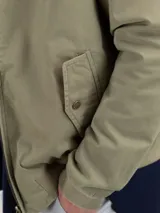 Cazadora tipo bomber color beige, con cierre frontal y bolsillos de solapa.