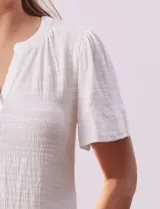 Remera blanca de poliéster, rayón y elastano, con cuello a la base y escote en V. Manga corta amplia bordada. Marca Cable & Gauge.