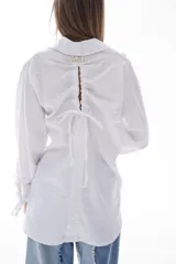 Camisa blanca de algodón con cuello clásico, mangas largas con puños fruncidos y cierre de botones al frente. Presenta frunces y lazo ajustable en la espalda.