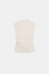 Top de algodón color beige, con cuello recto, mangas asimétricas y detalle de tejido drapeado en el lateral.