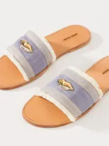 Sandalia chata confeccionada en denim, con flecos en la capellada y aplique metálico.