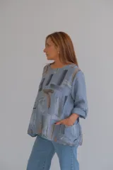 Blusa celeste con estampado abstracto en tonos grises y marrones, de corte holgado, mangas largas con puños abotonados y bolsillos delanteros.