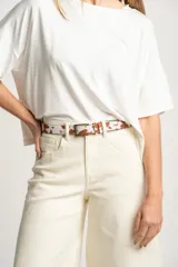 Cinto de cuero con estampado de vaca en tonos marrones y blancos, hebilla metálica color bronce.
